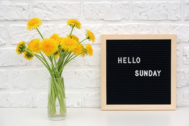 Hallo zondag woorden op zwarte letterboard en boeket gele paardebloemen bloemen op tafel