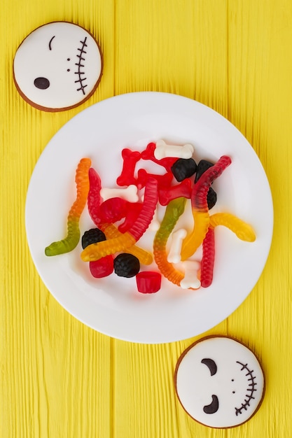 Halloween-achtergrond met koekjes en snoepjes bovenaanzicht op bord met kleurrijke gelei-snoepjes voor hallo...