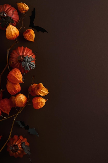 Halloween achtergrond zwerm zwarte vleermuizen en tak van droge oranje bloemen voor Halloween Zwarte papieren vleermuis silhouetten op bruine of donkere achtergrond herfst decoratie Halloween concept bovenaanzicht