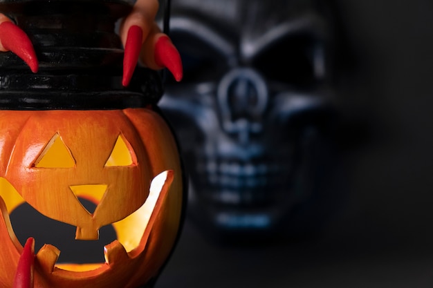 Halloween background glowing pumpkin and black skull on a dark background human fingers with long re...