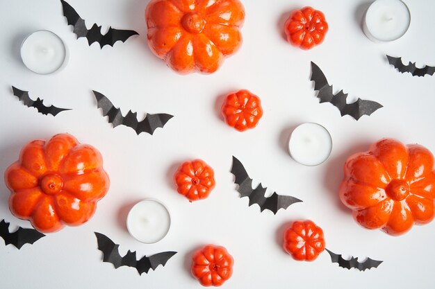 Halloween background, orange decorative plastic pumpkin black paper bat round candle white cardboard