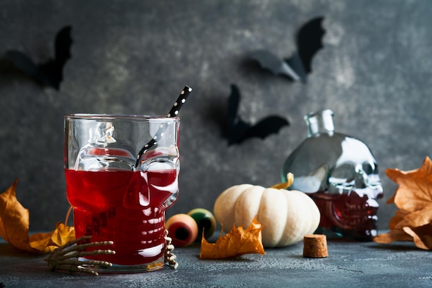 Halloween bloody cocktail Bloody red cocktail glass goblet for Halloween and bottle form skull on dark backgrounds Halloween party with candy eyes bats spiders Dia de los muertos Clousup