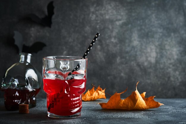 Halloween bloody cocktail Bloody red cocktail glass goblet for Halloween and bottle form skull on dark backgrounds Halloween party with candy eyes bats spiders Dia de los muertos Clousup