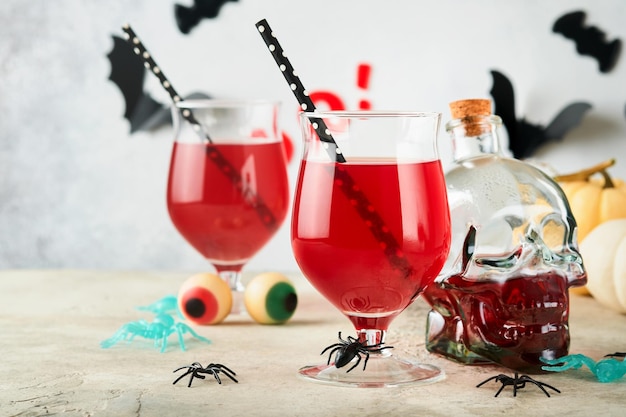 Cocktail sanguinanti di halloween due calici di vetro da cocktail sanguinanti per halloween e bottiglia a forma di teschio su sfondi chiari concetto di arredamento per la festa di halloween con occhi caramellati, pipistrelli, ragni e zucche