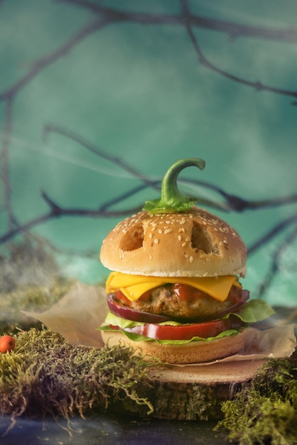 Halloween burger in a shape of pumpkin head jack lantern in a mystery forest. Scary cheeseburger