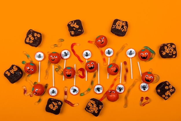 Photo halloween candy with black spiderscobwebsmiling pumpkins and tasty jelly worms on orange color