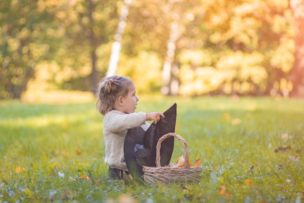 Concetto di celebrazione di halloween bambino carino che gioca con il cappello da strega sul prato nel parco autunnale su