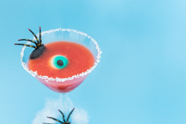 Halloween cocktail with spider and eye on blue background. Copy space.