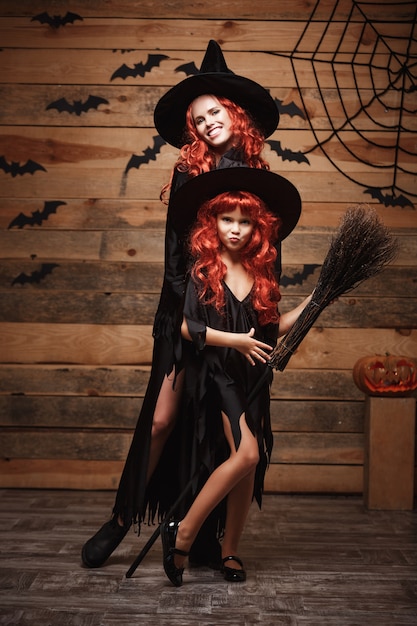 Halloween Concept - Beautiful caucasian mother and her daughter with long red hair in witch costumes celebrating Halloween posing 