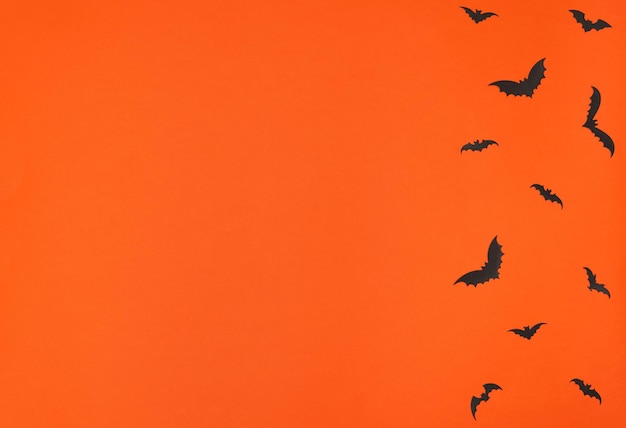 オレンジ色の背景の挨拶または招待状フラットレイスタイルのハロウィーンのコンセプトの黒い紙コウモリ