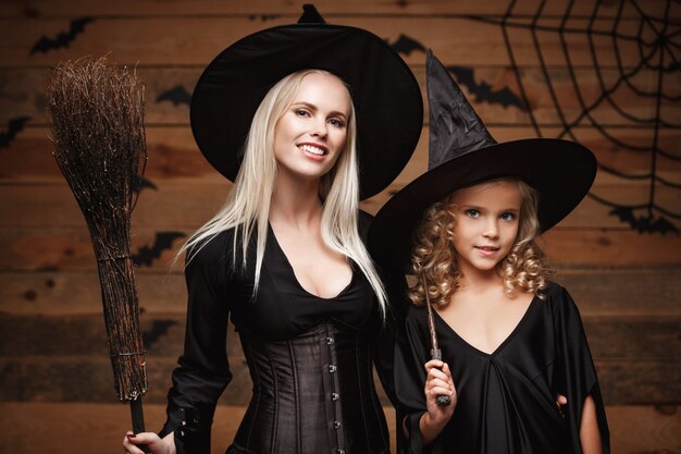 Halloween Concept - Closeup caucasian mother and her daughter in witch costumes celebrating Halloween posing on Wooden wall.