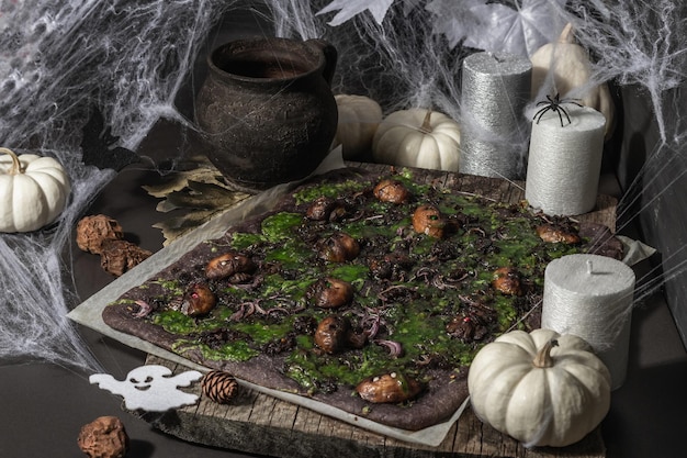 Halloween concept food. Flatbread or pizza with squid Ink, green cheese, mushrooms and purple onion. Bread of the Dead with festive decor, white pumpkin, candles and spider web. Dark stone background