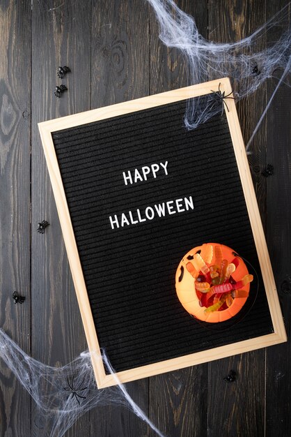 Halloween concept. Halloween party sweets with black letter board with words Happy Halloween flat lay on black wooden background with spider web