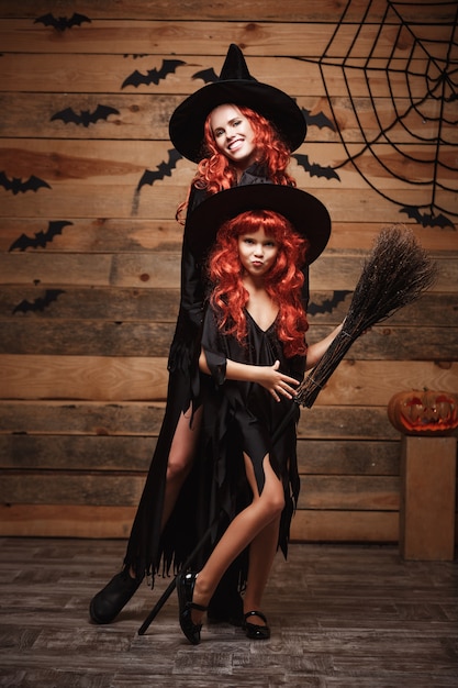 Halloween Concept - Mooie Kaukasische moeder en haar dochter met lang rood haar in heks kostuums vieren Halloween poseren