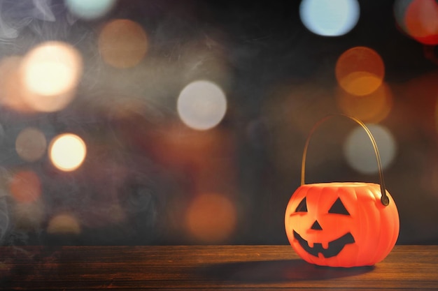 Halloween concept Orange plastic pumpkin lantern on a dark wooden table with blurry sparkling light in the background trick or treat close up