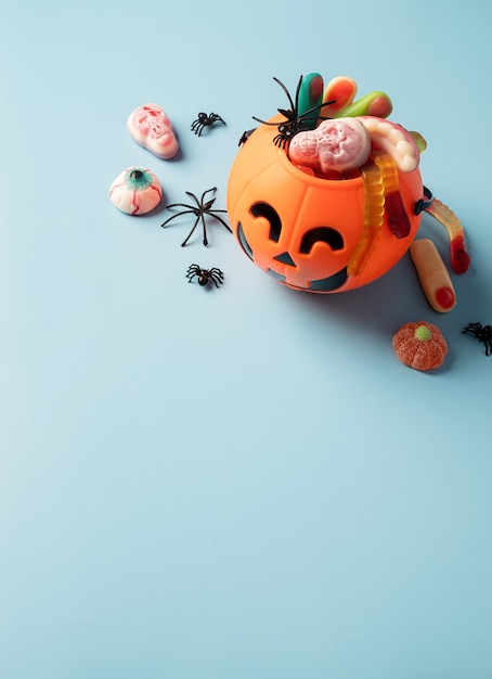 Halloween concept. Various halloween sweets in a pumpkin pot on blue solid background