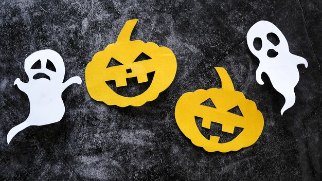 Halloween concept with pumpkins and ghosts cut paper on black concrete background.