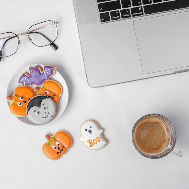 Halloween cookies hot coffee and computer laptop on white\
background happy halloween online shopping hello october fall\
autumn festive party and holiday concept