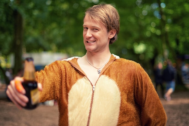 Halloween costume and man with beer to drink toast and happy celebration outdoor in bear outfit Animal suit and person smile in portrait with lager bottle and drunk from drinking alcohol in park