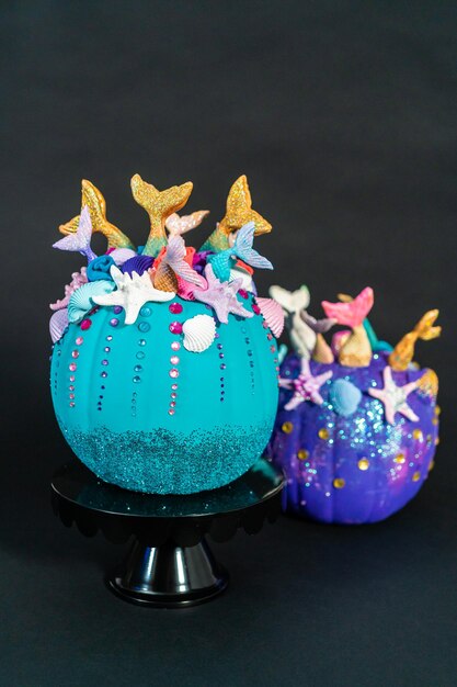 Halloween craft pumpkins decorated with mermaid tails, glitter, and sparkly rhinestones on a black background.