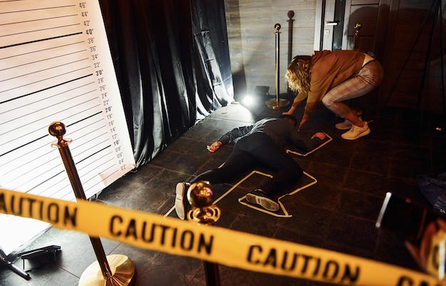 Foto scena del crimine di halloween del corpo sul pavimento e ragazza vicino a lui.