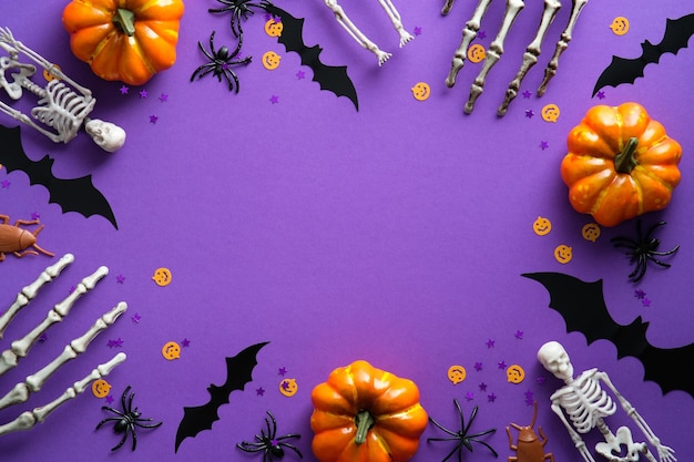 Halloween-decoraties op violette achtergrond Plat leggen Pompoenen Vleermuizen Spinnen Skeletten en Confetti
