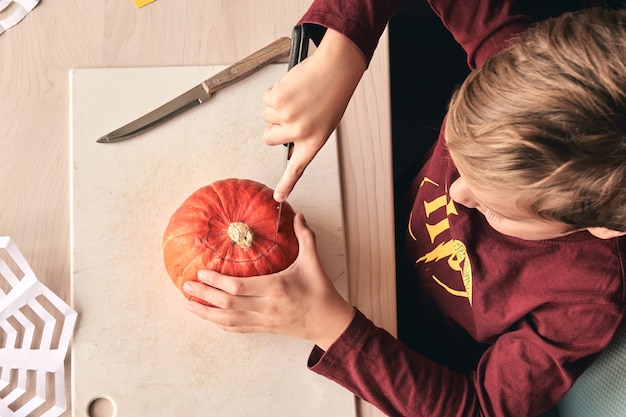 Idee per halloween, decorazioni e vacanze: primo piano di un bambino con zucca intagliata a coltello o jack-o-lantern. il ragazzo di 6 anni ha un'attività divertente in famiglia. la mamma trascorre del tempo con il figlio insieme