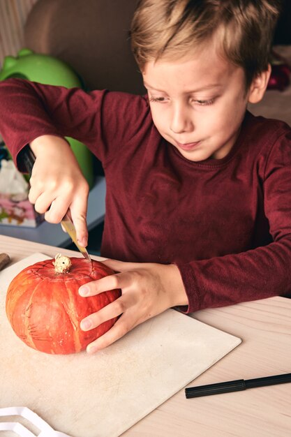 Idee per halloween, decorazioni e vacanze: primo piano di un bambino con zucca intagliata a coltello o jack-o-lantern. il ragazzo di 6 anni ha un'attività divertente in famiglia. la mamma trascorre del tempo con il figlio insieme