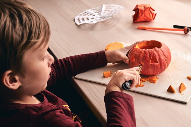 Halloween, decoration and holidays ideas- close up of kid with knife carving pumpkin or jack-o-lantern. 6 years boy has homefamily fun activity. Mom spending time with son together