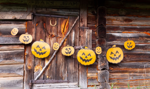 屋外のハロウィーンの装飾。村の古い銭湯の木製の壁にかわいいカボチャがぶら下がっている紙の花輪。