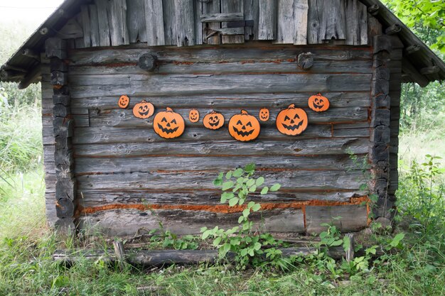 屋外のハロウィーンの装飾。村の古い銭湯の木製の壁にかわいいカボチャがぶら下がっている紙の花輪。