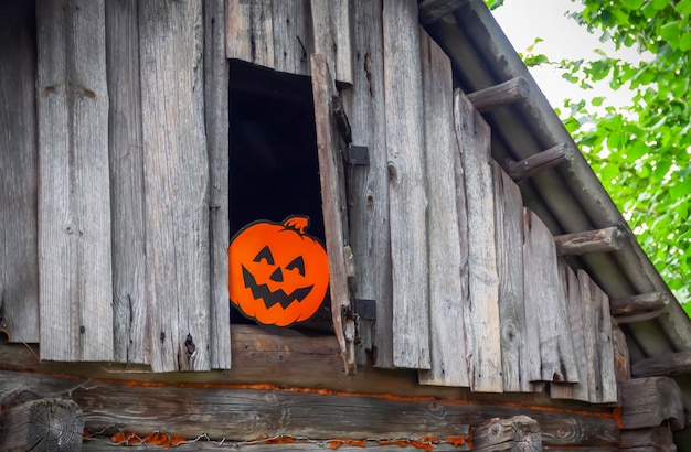 屋外のハロウィーンの装飾。村の古い銭湯の木製の壁にかわいいカボチャがぶら下がっている紙の花輪。