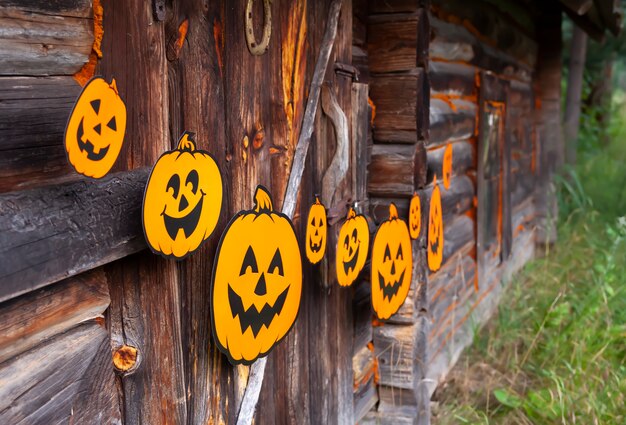 Halloween decoration outdoors. Paper garland with cute pumpkins hanging on the wooden wall of the old bathhouse building in village.