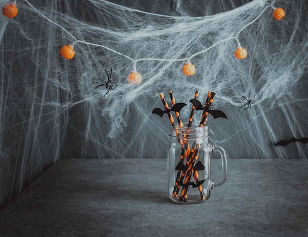 Halloween decorations A glass jar with drinking straws on dark background with cobwebs