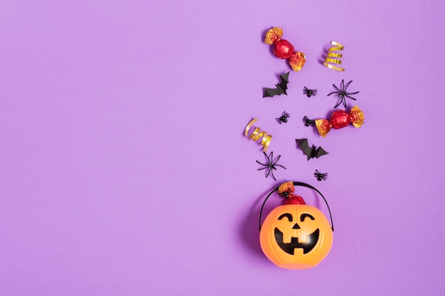 Halloween decorations paper bats flying from pumpkin bucket on purple background top view