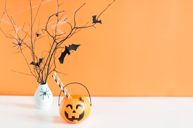 Хэллоуин украшения бумажные летучие мыши летают на ветке дерева и тыквенное ведро на оранжевом фоне
