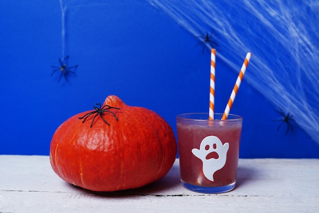 Halloween-drankjes met pompoen voor een kinderfeestje op wit hout en blauwe scène met spinnen