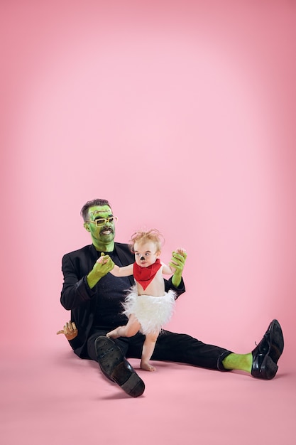 Famiglia di halloween. felice padre e bambini ragazza appena nata in costume di halloween e trucco. tema sanguinante: il pazzo maniaco su sfondo rosa dello studio