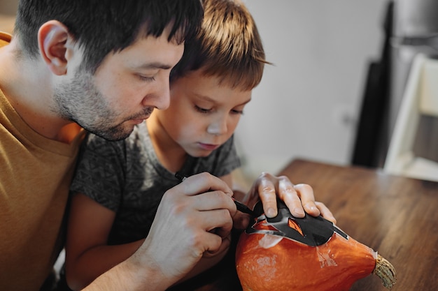 Halloween-feest voorbereiden. blanke man met zijn schattige 6-jarige zoon die ogen op een pompoen trekt om traditionele jack-lantaarn te maken. afbeelding met selectieve aandacht. hoge kwaliteit foto