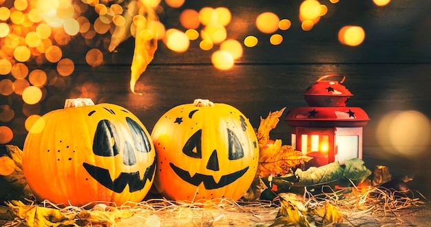 Halloween festive composition with smiling pumpkins guards with lights lantern straw and fallen leaves on dark wooden background rustic style selective focus