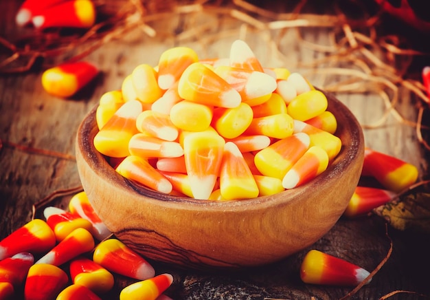 Halloween festive composition with sweet corn in bowl and smiling pumpkins guards lantern straw