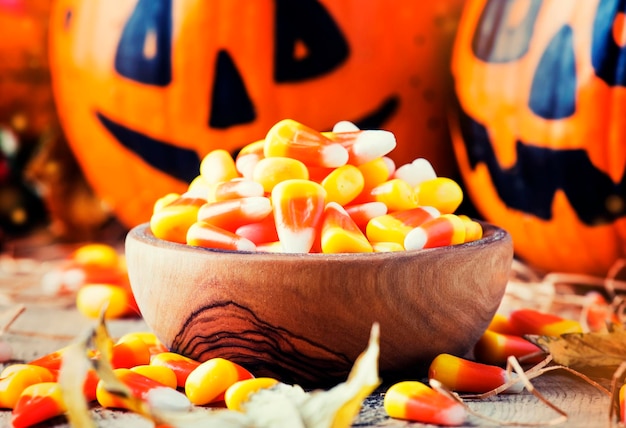 Halloween festive composition with sweet corn in bowl and smiling pumpkins guards lantern straw