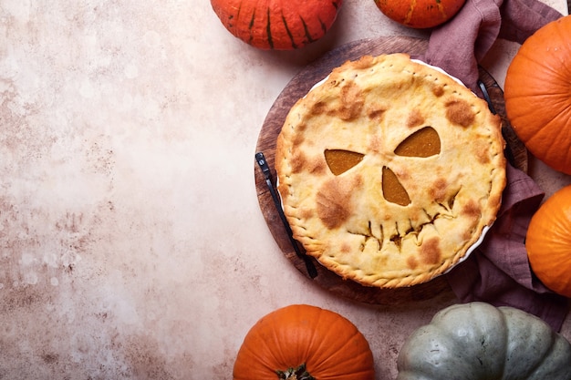 Halloween food. homemade pumpkin pie or tart with a scary face\
for halloween on a wooden table. copy space. halloween food\
concept.