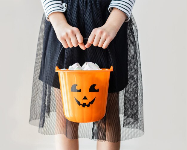 Photo halloween a girl dressed as a witch is holding a pumpkin bucket full of sweets trick or treat