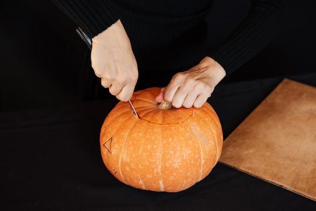 Halloween. Girl's hands with a knife cutting orange pumpkin for making Jack's lantern
