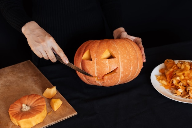 Halloween. Girl's hands with a knife cutting orange pumpkin for making Jack's lantern