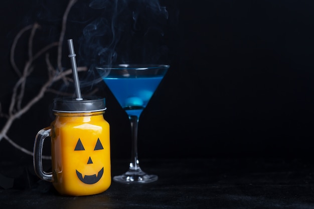 黒い背景に怖い顔でガラスの瓶にハロウィーンの健康的なカボチャやニンジンを飲む