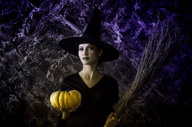 Halloween-heks die een pompoen en een bezem houdt. vrouw gekleed als een feeënheks