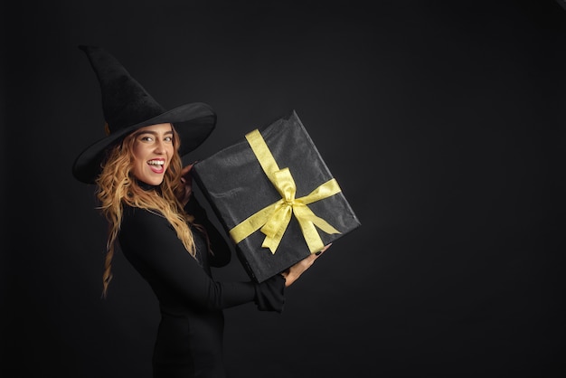 Halloween-heks met een zwarte hoed op een zwarte muur met geschenkdozen