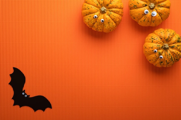 Halloween holiday background Orange pumpkin bat with funny eyes spider spider web old leaves and branches from scary forest on orange background Happy Halloween card Autumn decoration Top view